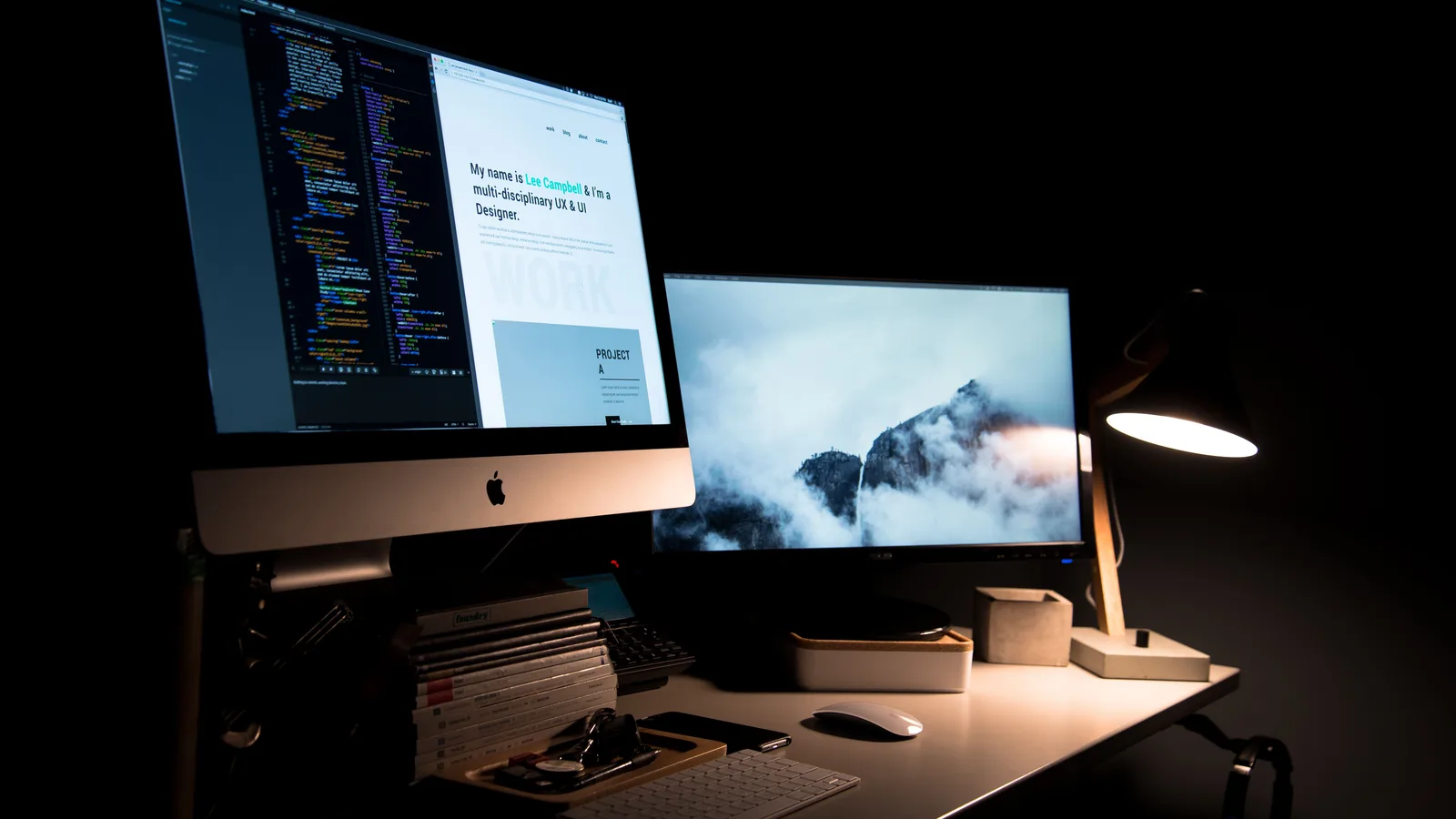 A clean and stylish workspace featuring dual monitors, a lamp, and office supplies.