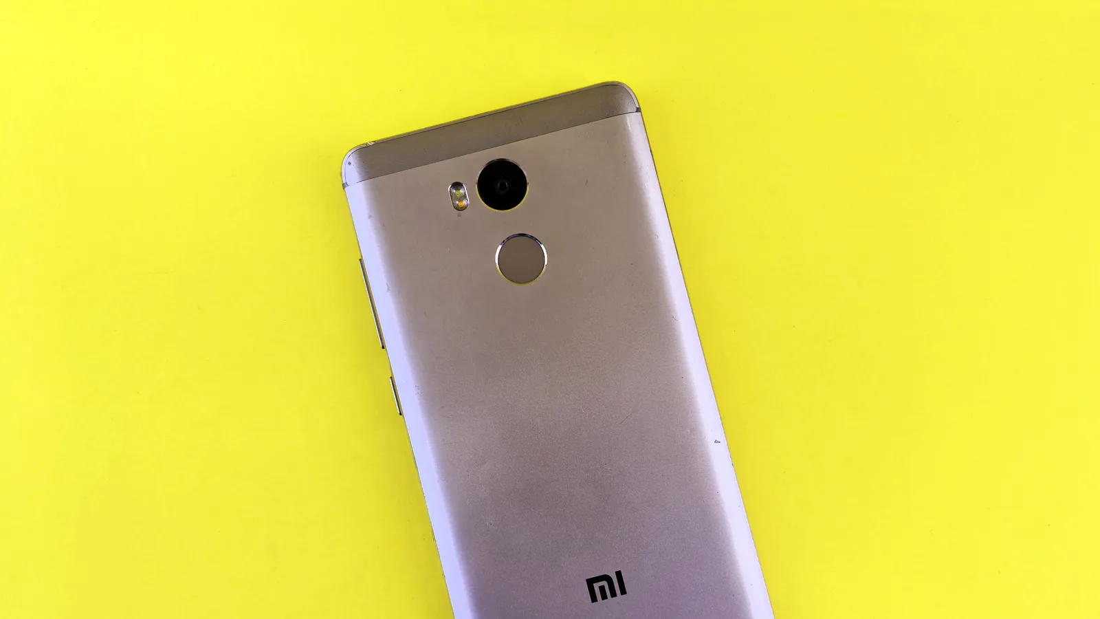 A silver smartphone placed on a bright yellow background, showcasing sleek design.