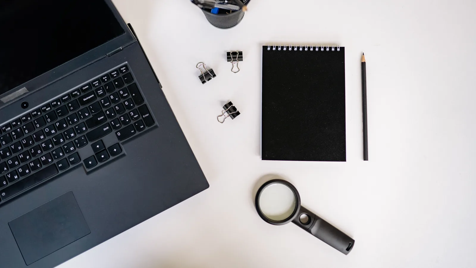 Flat lay of black office supplies on white background, including laptop and notepad.