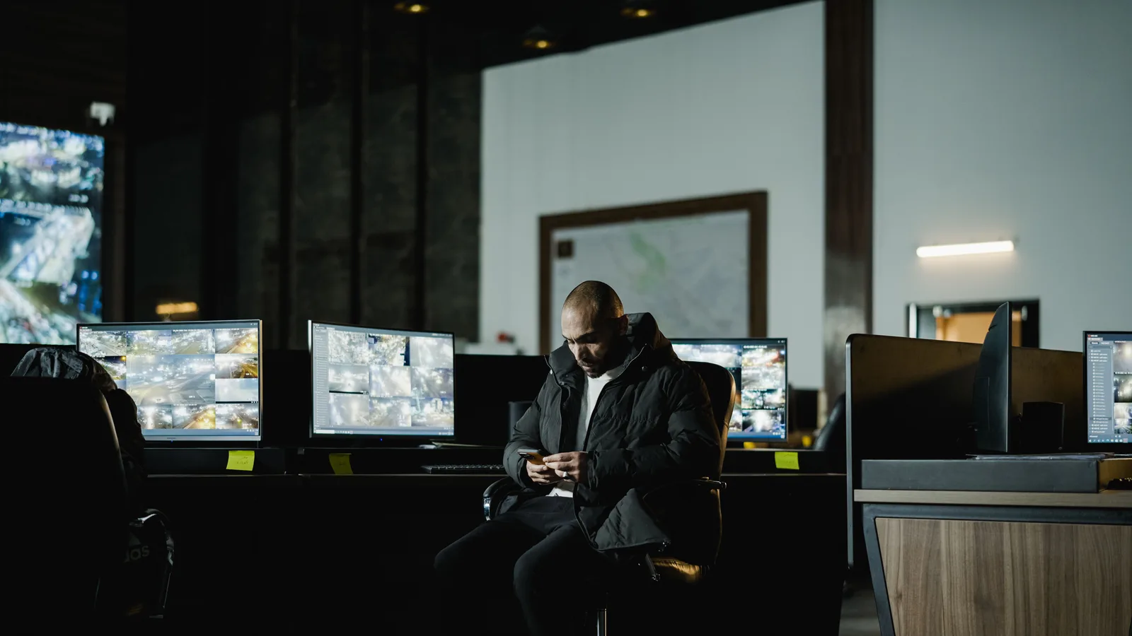 Security officer seated in a dimly lit control room, analyzing multiple surveillance screens.