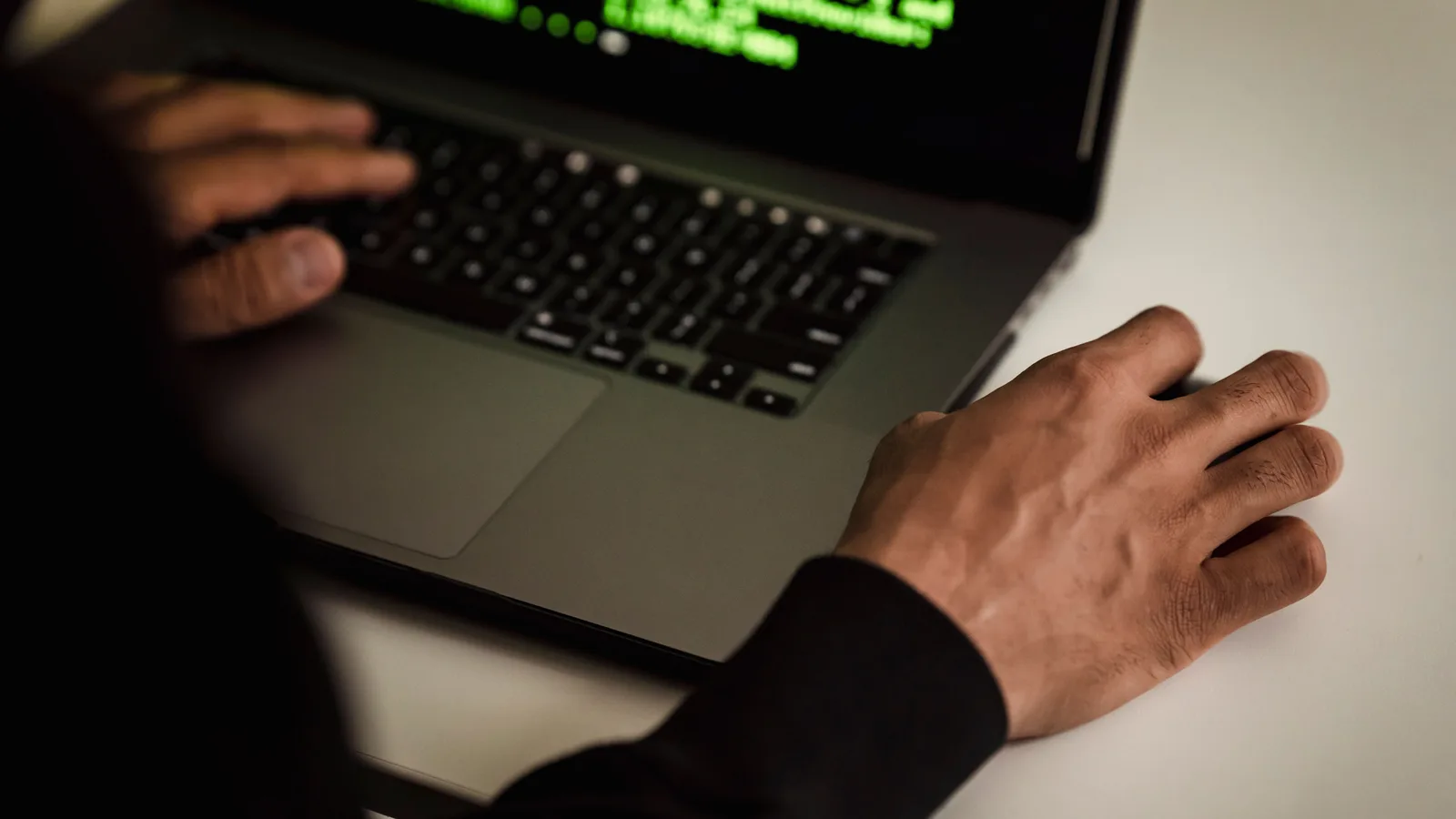 From above crop faceless male developer in black hoodie writing software code on netbook while working in light studio