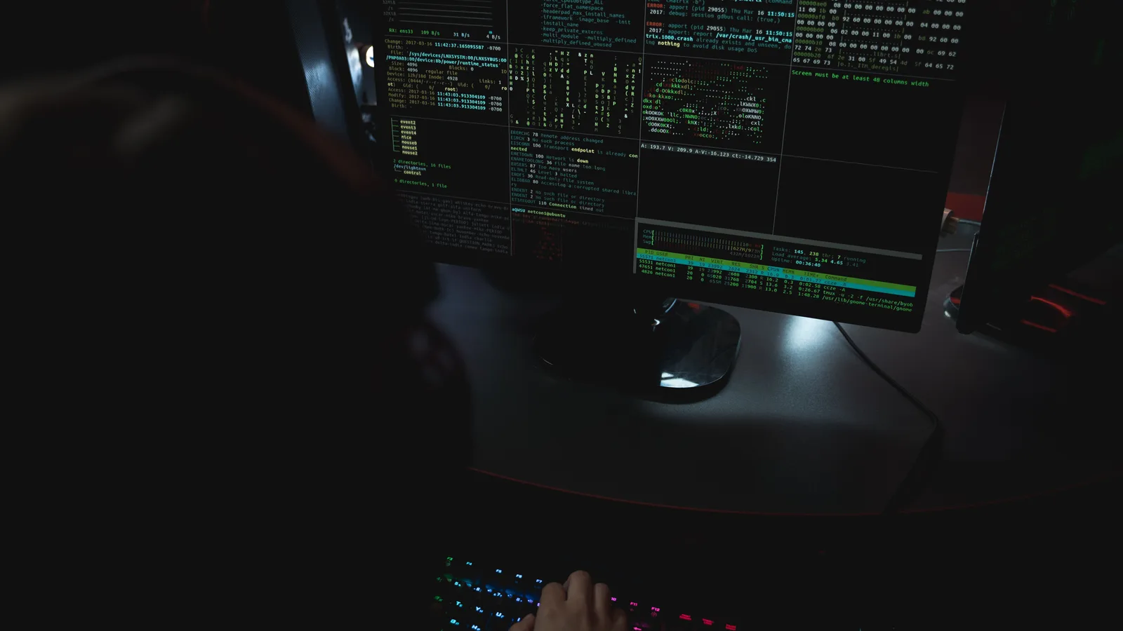 Dark room setup with code displayed on PC monitors highlighting cybersecurity themes.