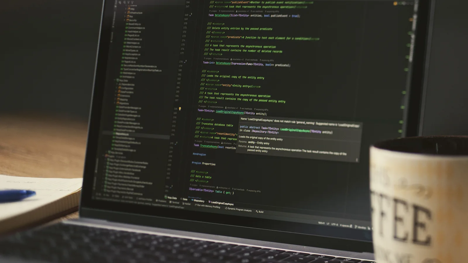 A close-up of a laptop displaying code in a dimly lit room with a coffee mug nearby.